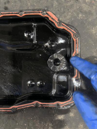 Technician at BR Prestige Auto pointing to accumulated metallic wear particles on the magnet inside a 2007 Mazda 5 transmission pan in Peachtree Corners, GA